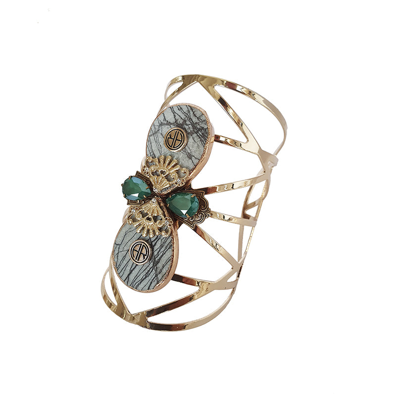 alt= "Statement cuff featuring Adrienne Reid signature branding including Swarovski Crystals in emerald with raw labrodite and gold detailing"
